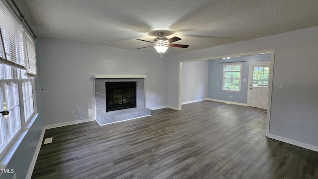 unfurnished living room featuring a brick fireplace, a textured ceiling, dark wood-type flooring, and ceiling fan