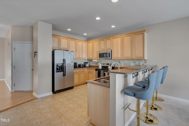 kitchen with stainless steel appliances, kitchen peninsula, light brown cabinets, dark stone countertops, and backsplash