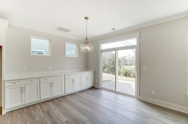 unfurnished dining area with an inviting chandelier, crown molding, a healthy amount of sunlight, and light wood-type flooring