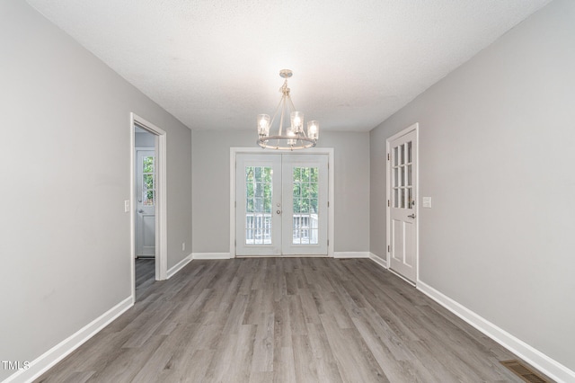 unfurnished room featuring french doors, a chandelier, a textured ceiling, and light wood-type flooring