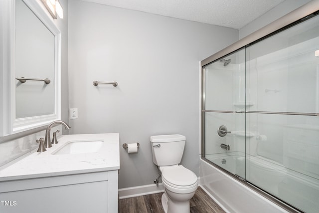 full bathroom featuring hardwood / wood-style floors, vanity, bath / shower combo with glass door, toilet, and a textured ceiling