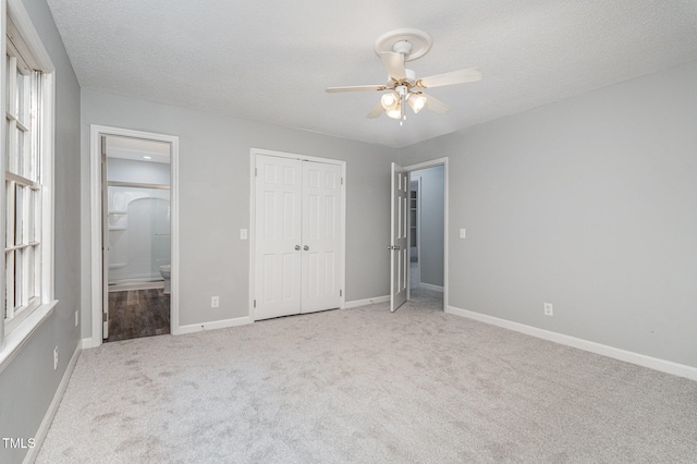 unfurnished bedroom with light carpet, ceiling fan, a textured ceiling, connected bathroom, and a closet