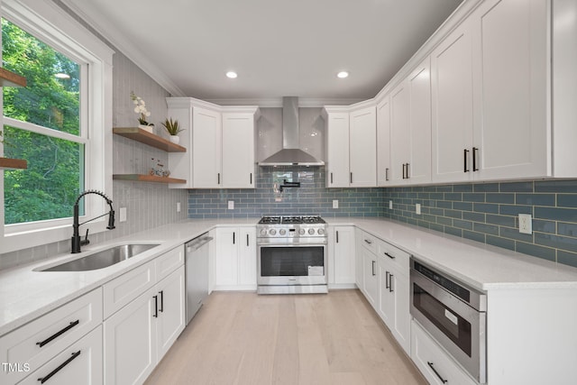 kitchen with sink, wall chimney exhaust hood, decorative backsplash, white cabinets, and appliances with stainless steel finishes