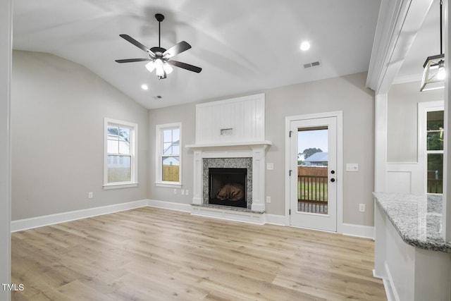 unfurnished living room featuring lofted ceiling, a ceiling fan, a fireplace with raised hearth, visible vents, and light wood-type flooring