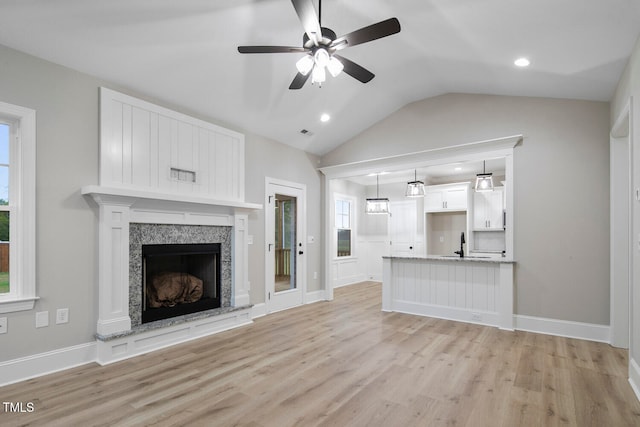 unfurnished living room with light hardwood / wood-style flooring, a high end fireplace, lofted ceiling, and ceiling fan