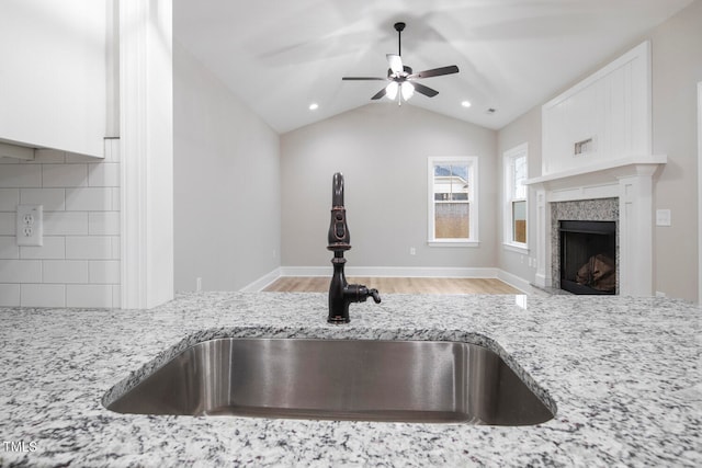 kitchen with light stone countertops, sink, backsplash, lofted ceiling, and white cabinets