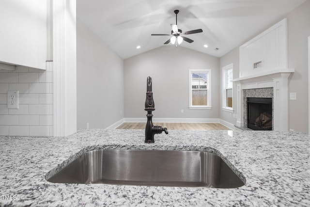 room details featuring a ceiling fan, a sink, light wood-type flooring, light stone countertops, and backsplash