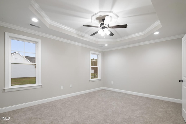 spare room featuring carpet, a tray ceiling, visible vents, ceiling fan, and ornamental molding