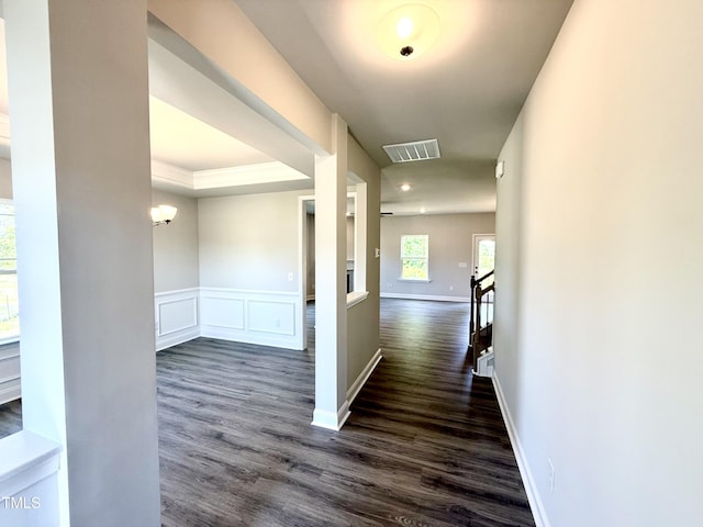 hallway with visible vents, wainscoting, a decorative wall, baseboards, and dark wood-style floors