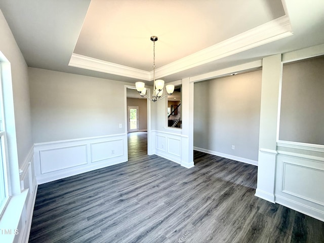 unfurnished dining area with crown molding, a raised ceiling, a decorative wall, a chandelier, and dark wood finished floors