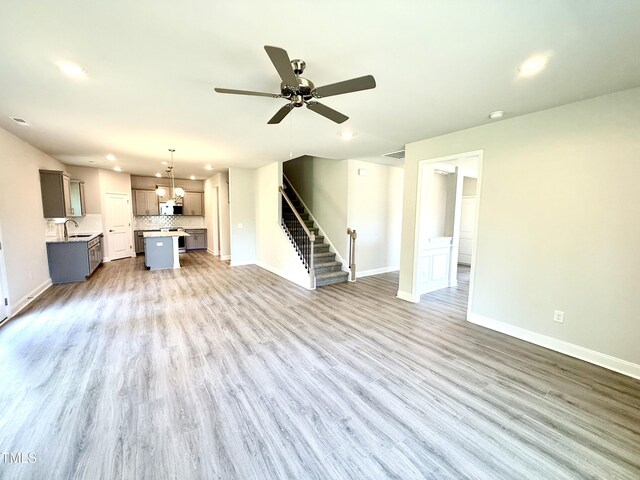 unfurnished living room with stairway, baseboards, a sink, and wood finished floors