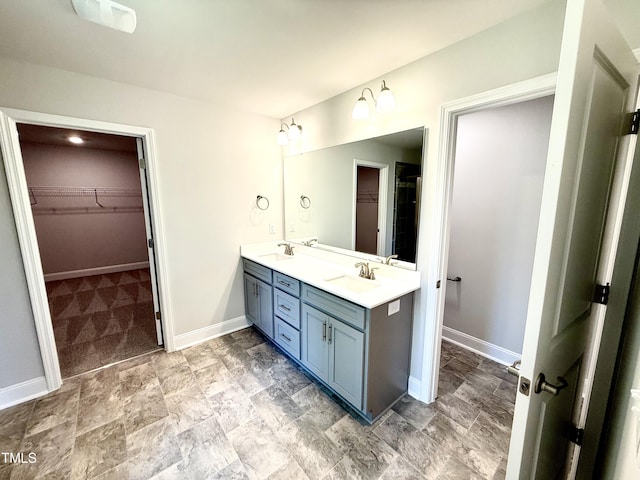 bathroom with a sink, baseboards, double vanity, and a spacious closet