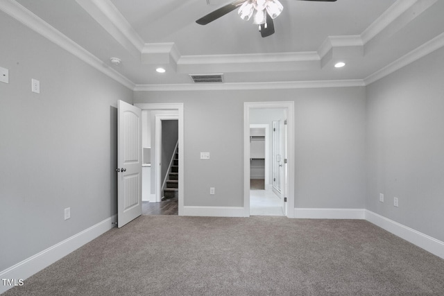 unfurnished bedroom featuring a spacious closet, ornamental molding, light carpet, a raised ceiling, and ceiling fan