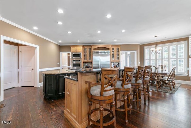 kitchen with a center island, ornamental molding, pendant lighting, built in appliances, and dark wood-type flooring