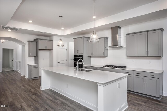 kitchen with gray cabinetry, dark wood-type flooring, sink, wall chimney exhaust hood, and an island with sink