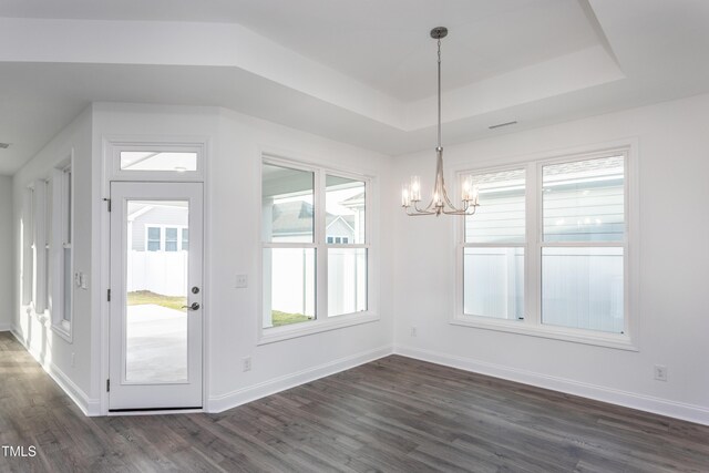 unfurnished dining area featuring a notable chandelier, dark hardwood / wood-style floors, and a tray ceiling