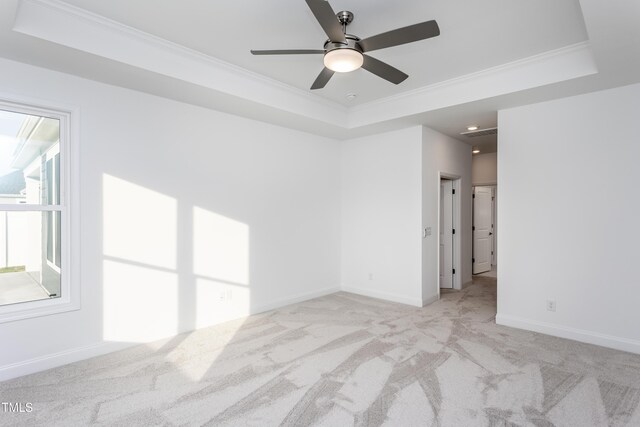 spare room with a raised ceiling, light carpet, ceiling fan, and ornamental molding