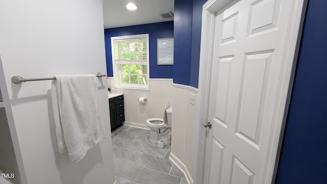 half bathroom featuring vanity, a wainscoted wall, visible vents, and toilet