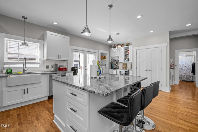 kitchen with sink, a kitchen island, a kitchen breakfast bar, light hardwood / wood-style floors, and white cabinets