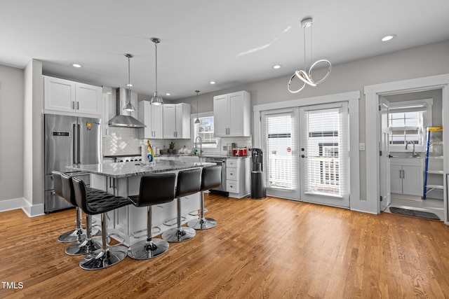 kitchen with white cabinetry, wall chimney range hood, appliances with stainless steel finishes, and a wealth of natural light