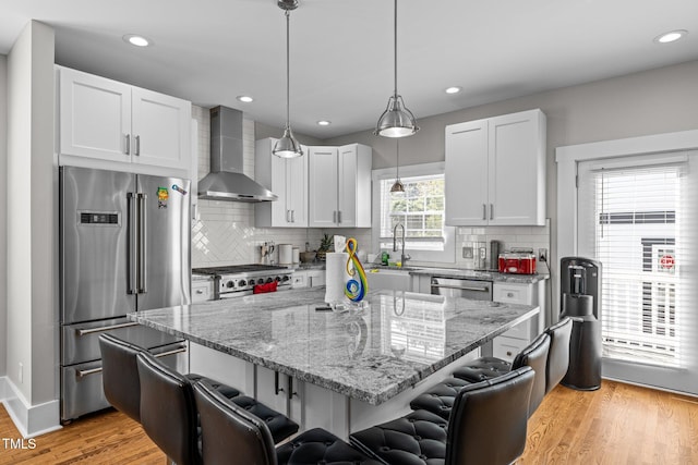 kitchen featuring a kitchen breakfast bar, wall chimney exhaust hood, white cabinetry, and high quality appliances