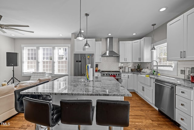 kitchen with premium appliances, a center island, white cabinetry, wall chimney exhaust hood, and a breakfast bar area