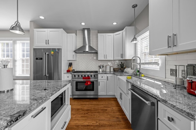 kitchen featuring wall chimney range hood, white cabinets, premium appliances, and plenty of natural light