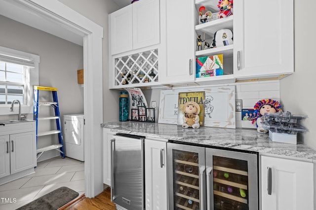 bar with beverage cooler, white cabinets, light stone counters, stainless steel refrigerator, and light tile patterned floors