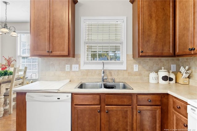 kitchen with white dishwasher, sink, decorative backsplash, and hanging light fixtures