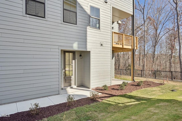 view of exterior entry featuring a lawn and a balcony