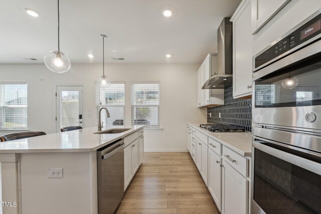 kitchen featuring a healthy amount of sunlight, sink, stainless steel appliances, wall chimney exhaust hood, and a kitchen island with sink