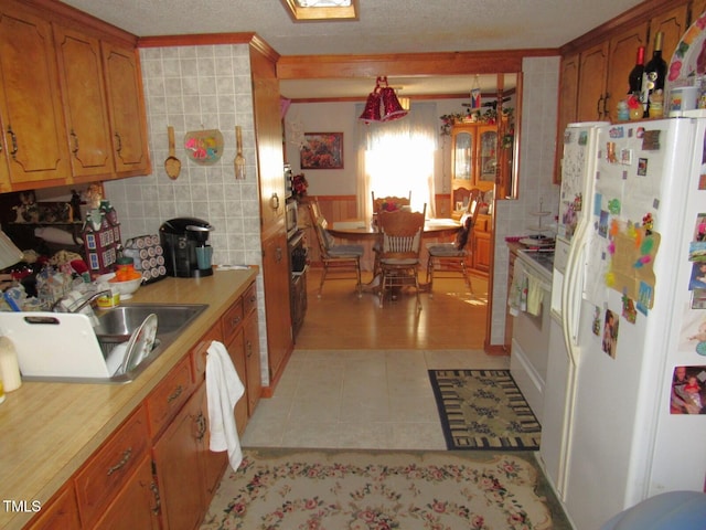 kitchen with ornamental molding, sink, white refrigerator with ice dispenser, pendant lighting, and light tile patterned floors