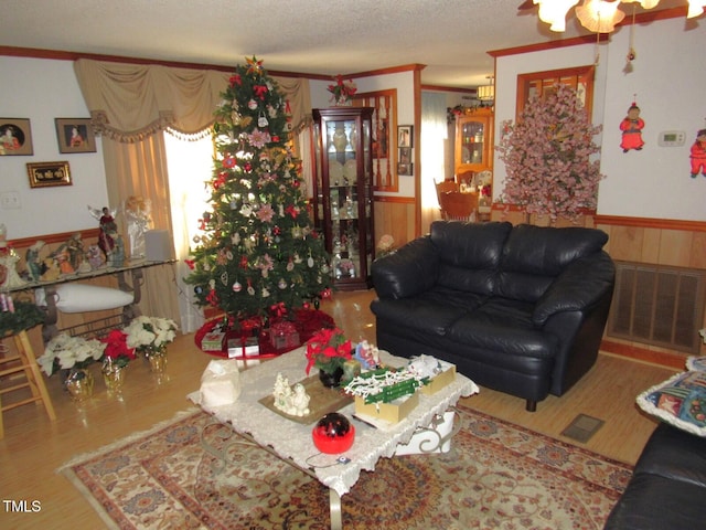 living room with hardwood / wood-style flooring, a textured ceiling, ornamental molding, and wooden walls