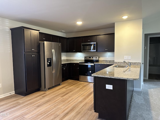 kitchen featuring appliances with stainless steel finishes, sink, kitchen peninsula, light stone counters, and light hardwood / wood-style flooring