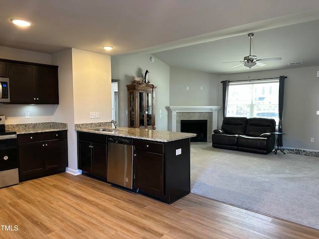 kitchen featuring kitchen peninsula, a tiled fireplace, ceiling fan, appliances with stainless steel finishes, and light hardwood / wood-style floors