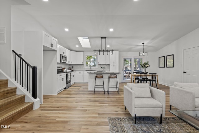 living room featuring sink, lofted ceiling with skylight, light hardwood / wood-style flooring, and a chandelier