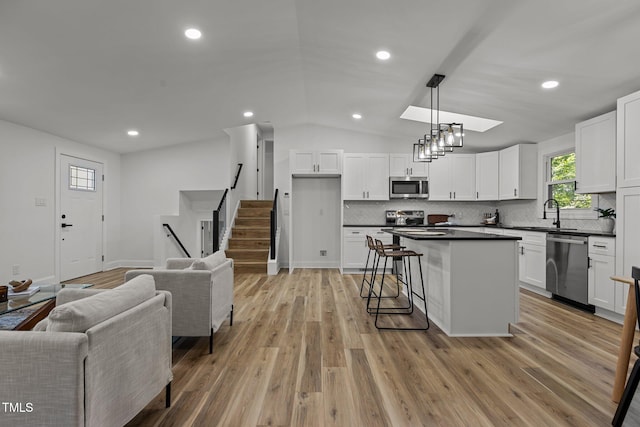 kitchen with white cabinets, appliances with stainless steel finishes, light hardwood / wood-style flooring, lofted ceiling with skylight, and decorative light fixtures