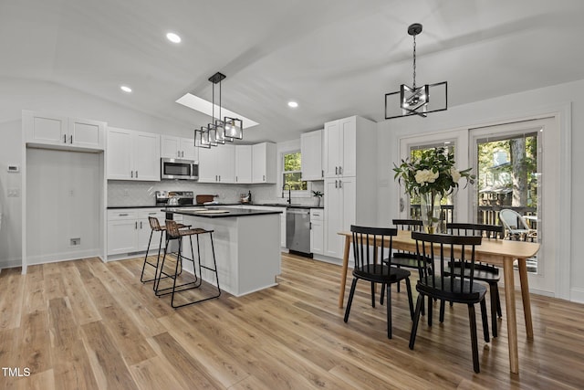 kitchen featuring white cabinets, hanging light fixtures, vaulted ceiling with skylight, stainless steel appliances, and light hardwood / wood-style floors