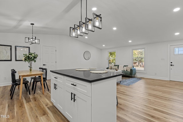 kitchen with light wood-type flooring, a center island, vaulted ceiling, decorative light fixtures, and white cabinets