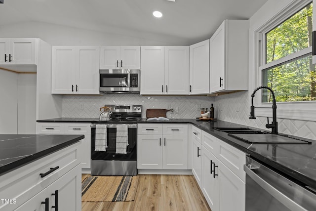 kitchen featuring tasteful backsplash, white cabinetry, vaulted ceiling, sink, and stainless steel appliances