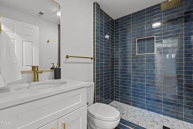 bathroom with vanity, a tile shower, toilet, and tile patterned flooring