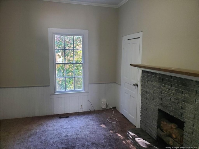 unfurnished living room featuring crown molding, a brick fireplace, dark colored carpet, and wooden walls