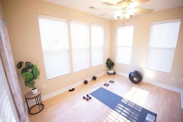 workout area featuring light wood-style floors, a ceiling fan, visible vents, and baseboards