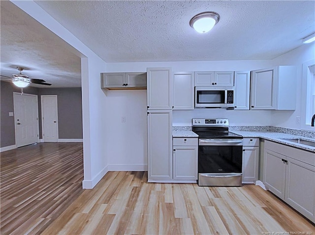 kitchen with stainless steel appliances, sink, light wood-type flooring, and ceiling fan