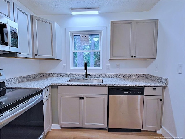 kitchen featuring light hardwood / wood-style flooring, stainless steel appliances, sink, light stone countertops, and a textured ceiling