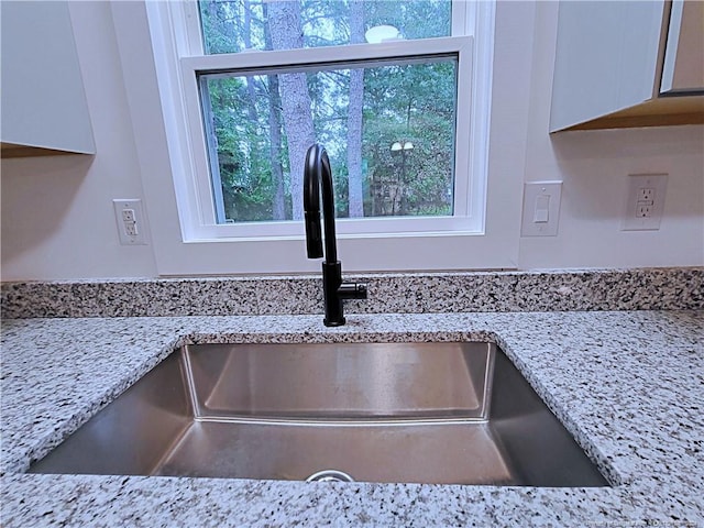 details with sink, light stone countertops, and white cabinets