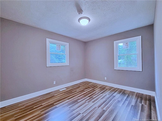 empty room with a wealth of natural light, hardwood / wood-style floors, and a textured ceiling