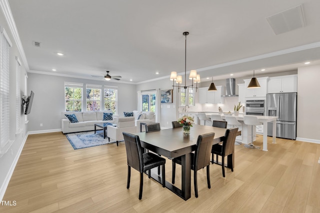 dining room featuring light hardwood / wood-style floors, crown molding, and ceiling fan with notable chandelier