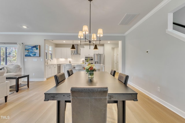 dining space featuring a chandelier, sink, crown molding, and light wood-type flooring