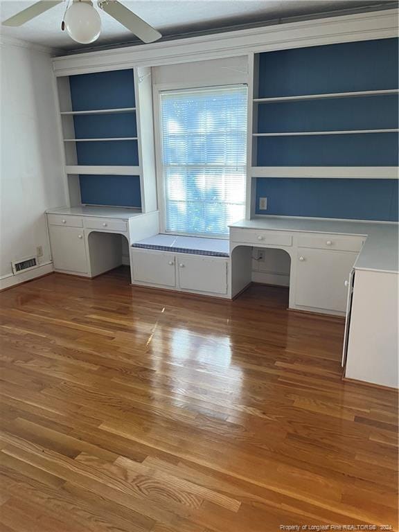 unfurnished office featuring built in desk, wood-type flooring, and ceiling fan